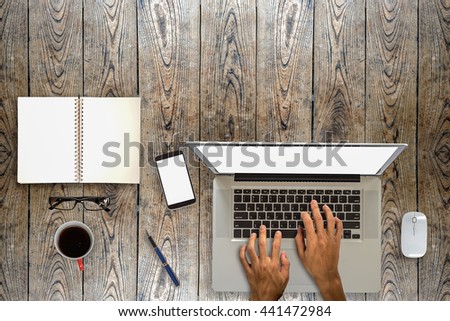 A man is working by using a laptop computer on vintage wooden table. Hands typing on a keyboard. Top view.
