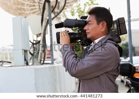 News cameraman broadcasting filming outdoor event.