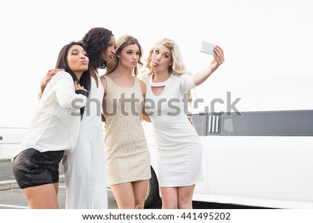 Well dressed women taking a selfie next to a limousine on a night out