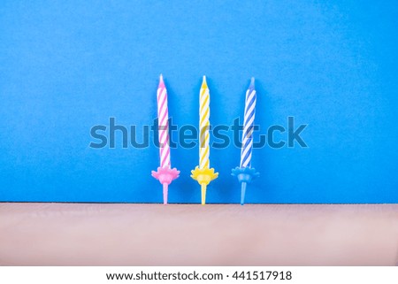 Three colorful birthday candles in a row on blue background