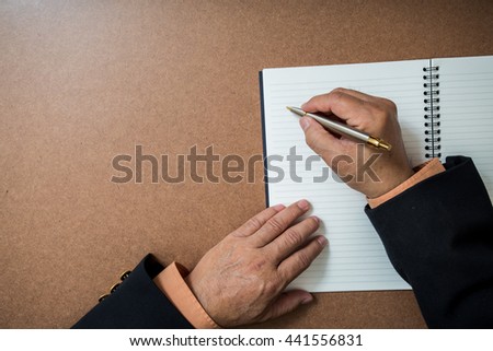 A business man  is writing in a big notepad on a wooden table