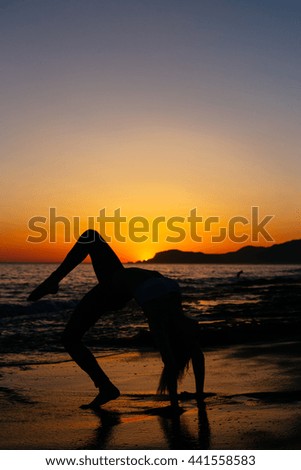 Girl practicing acrobatics yoga on beach of mediterranean sea during sunset 