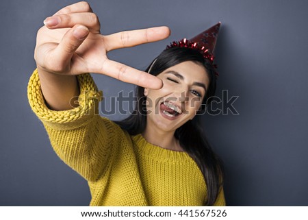 Portrait of brunette showing tongue and peace sign while wearing red festive hat