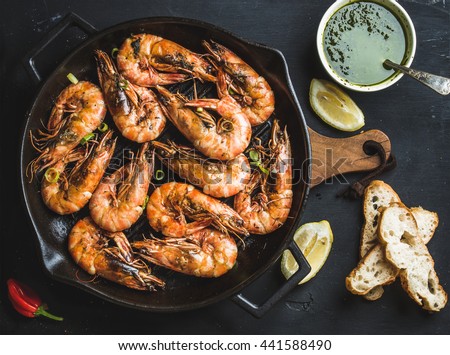 Roasted tiger prawns in iron grilling pan with fresh leek, lemon, bread and pesto sauce over black background, top view Royalty-Free Stock Photo #441588490