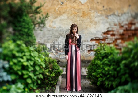 A view on the seductive woman in pink standing among the green bushes