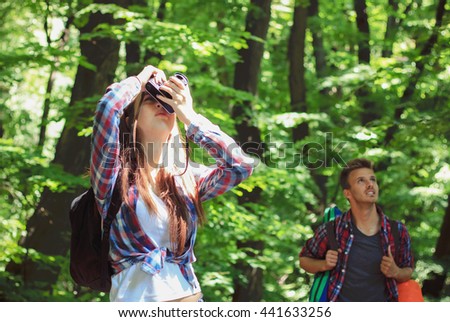 Portrait of a young girl taking a photo in forest with her boyfriend on the background. Camping, hiking.
