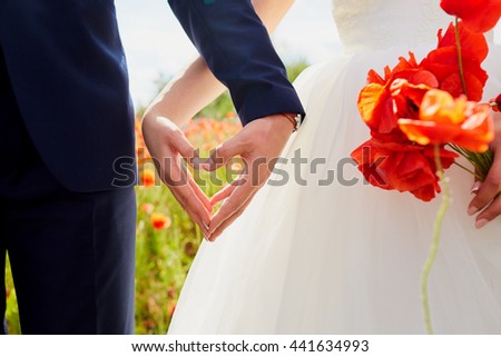 Hands of bride and groom in a shape of heart. Wedding ,love,heartconcept. In the hands of the bride bouquet of poppies. Wedding couple in the poppy field.