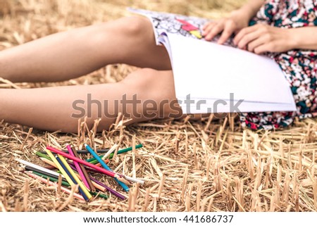 sitting on the hay and coloring, with different bright pencils, colorful dress and slim legs and hat