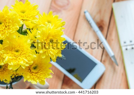Yellow chrysanthemum flowers next to smart phone with pen soft focus on wooden table. vintage filtered and toned