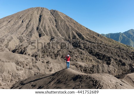 Lone female tourist taking picture of beautiful desert volcano mountain during blue sky.