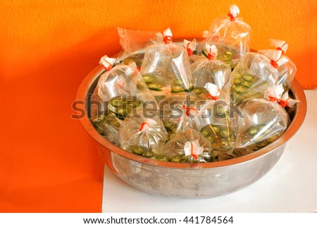 group of bags contained vinegar and green chili sealed with rubber band in a stainless steel bowl on a white table with orange wall painted background