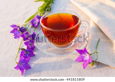 English tea in the garden. Cup of tea served on the linen tablecloth with blue bell flowers in the garden. Rustic tea time concept. 