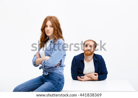 Beautiful redhead girl and boy posing over white background. Boy sitting at white table. Girl sitting on table.