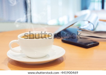 White cup of coffee with magazine and tablet computer on wood table in cafe. Selective focus.