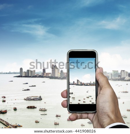 Mobile phone on hand with cityscape view and blue sky, taking photo of the city