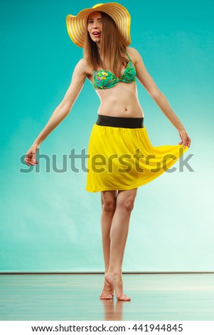 Holidays and summer fashion. Woman wearing yellow hat and bikini. Female model posing in full length on blue background.