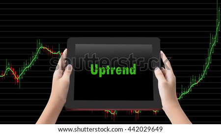 Financial Concept. " Uptrend" words in green color on tabled in hands and technical bar chart  background.
