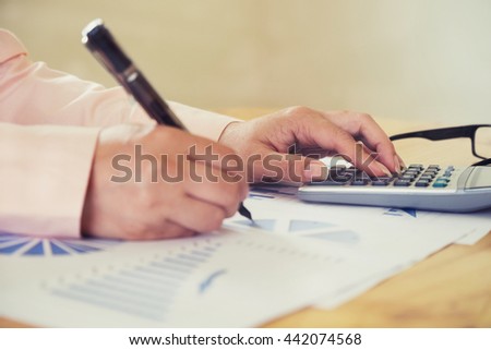 Female office worker typing on the keyboard and using a calculator to calculate the numbers vintage tone
