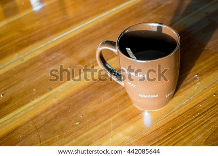 The cup of coffee in the high contrast between dark shade and light of the sun in the morning on wooden table , these made this picture keep yellow or light brown color theme.