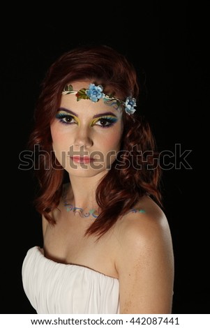Beautiful portrait of a lovely redhead model with long curly hair and fairy type avant-garde makeup, wearing a white strapless dress on a black background