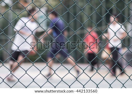 Steel wire mesh fence with People playing basketball court blur background.
