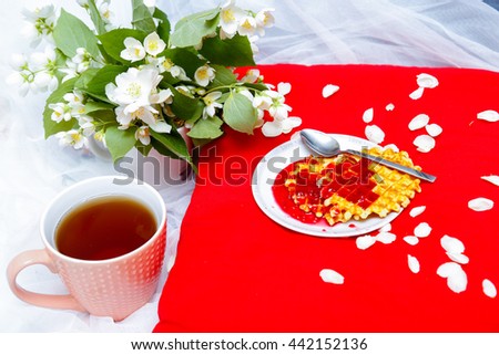 Breakfast in bed -tea and biscuits with strawberry jam on red pillow, jasmine flowers