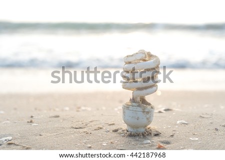 Light bulb was thrown away on the beach and free form copy space. Environmental pollution concept picture.