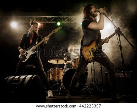 Rock band performs on stage. Guitarist, bass guitar and drums. The guitarist plays solo. Royalty-Free Stock Photo #442225357
