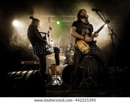 Rock band performs on stage. Guitarist, bass guitar and drums. The guitarist plays solo. Royalty-Free Stock Photo #442225390