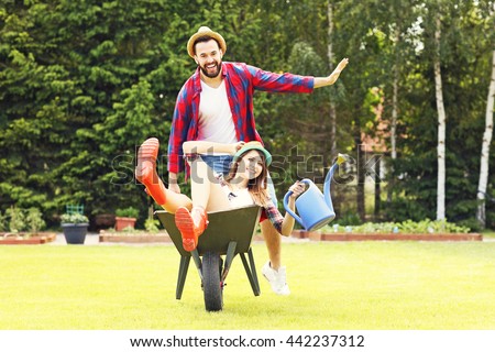 Picture of young couple having fun in the garden riding a barrow