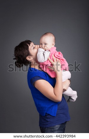 Happy mother embraces her little daughter on gray background