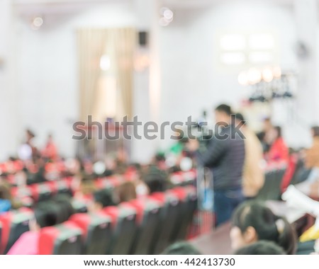 Blurred abstract of cameraman recording/videotaping an event in the university hall in Hanoi, Vietnam. Campus lecture hall with full of audience in line of red armchairs rows. Blur people background.