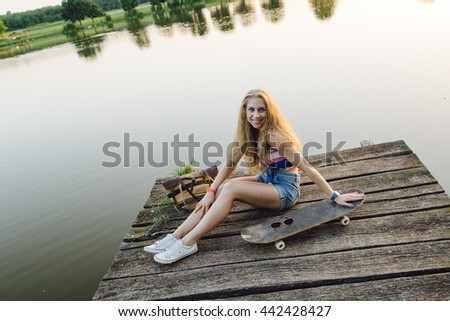 Cute girl resting by the lake with skateboard at sunset