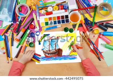Vintage sailboat galleon and island, child drawing, top view hands with pencil painting picture on paper, artwork workplace