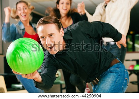 Group of four friends in a bowling alley having fun, three of them cheering the one in charge to throw the ball