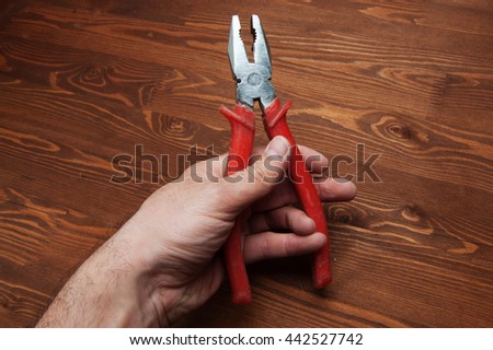 against the background of a wooden tabletop, pliers in a man's hand.