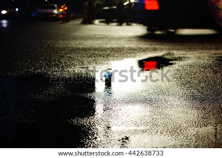 Rainy night in the big city, the light from the headlamps of vehicles approaching on the road. Close up view from the level of asphalt, focus on the asphalt