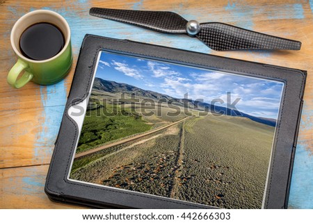 reviewing aerial picture on a digital tablet with a cup of coffee - foothills of Medicine Bow Mountains with a dirt road and cattle, North park, Colorado