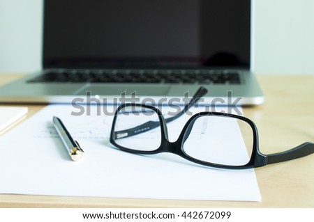 Close up eyeglass on paper report and blur laptop background