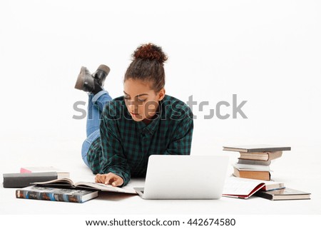 Portrait of young beautiful african girl with laptop and books reading over white background.