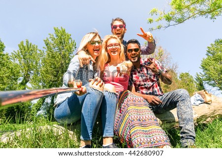 Group of multiracial friends taking selfie with stick sitting on old tree trunk - Mixed race students having fun at green park - Concept of joyful moment on sunny spring day -  Bright Vintage filter