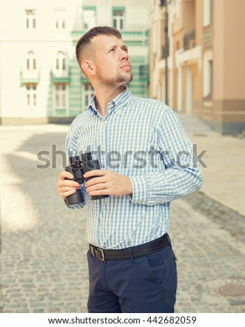Young man holding binoculars in hand, but looks the other way.