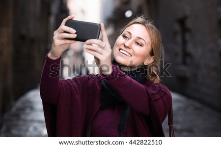 Cheerful girl looking curious and taking pictures with her phone outdoors

