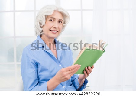 Photo of beautiful emotional adult woman. White interior with window. Woman reading book