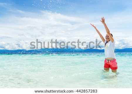 young beautifull girl playing with turquoise water at tropical island under blue sky