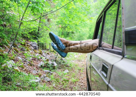 Young woman enjoying to the travel in the nice forest with her boyfriends classic car. With blue shoes.