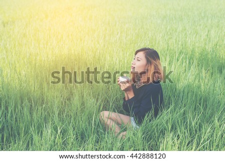 Young hipster woman sitting on green grass holding hot coffee and enjoy fresh air in the morning.