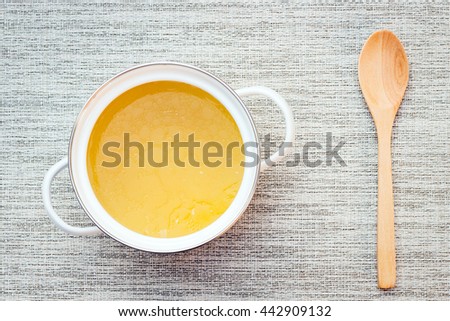 Bowl of chicken broth on gray table mat with wooden spoon