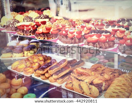 Sweet baked goods behind a window of a bakery. Delicious eclairs, waffles, muffins and donuts behind a shop window.