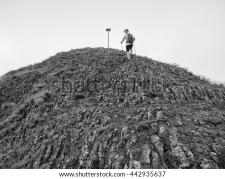 Hiker climbing on sharp peak of basalt formation. Long basalt poles of cold volcano. Black and white photo